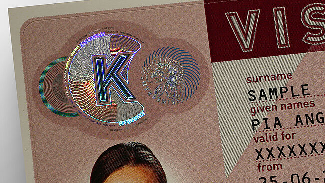 Imagen de un parche de KINEGRAM de muestra con una letra K metalizada y líneas metalizadas que se convierten en líneas azules impresas