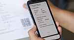 Image de mains tenant un smartphone pour scanner le code QR sur un document en papier