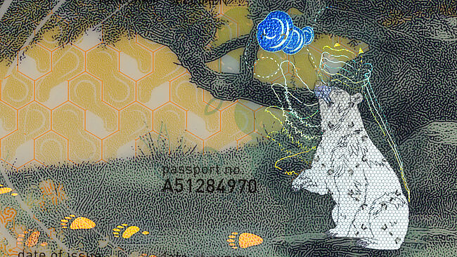 Close-up image of part of a sample passport data page with a KINEGRAM PCI with Full Data Protection security feature whose motifs show a bear stealing honey from a beehive. The close-up focuses on the bear.