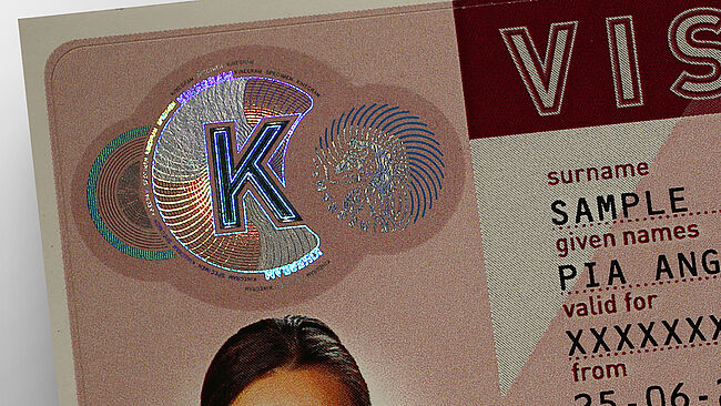 Image of a sample KINEGRAM patch with a metallized letter K and metallized lines that transform into printed blue lines