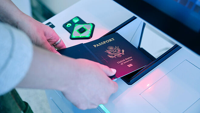 Image showing the inspection of a passport by a machine, the data page is held over the camera zone of the machine.
