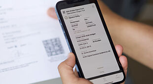 Imagen de manos que sostienen un teléfono inteligente y escanean el código QR seguro en un documento