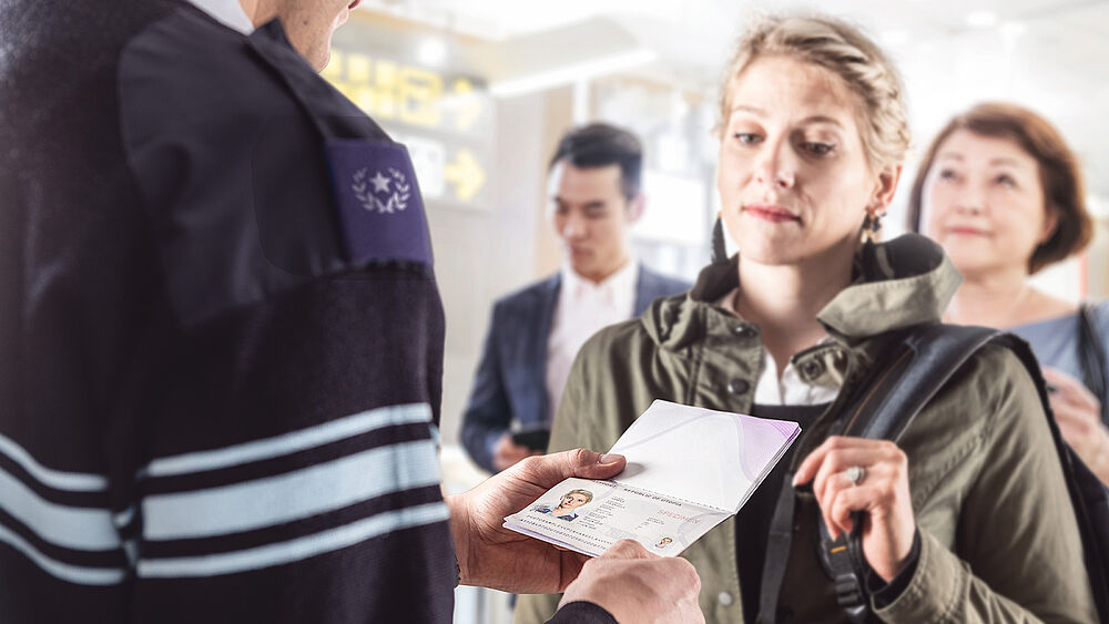 Image showing a group of persons in front of an officer, one of the persons is handing over her passport for inspection.